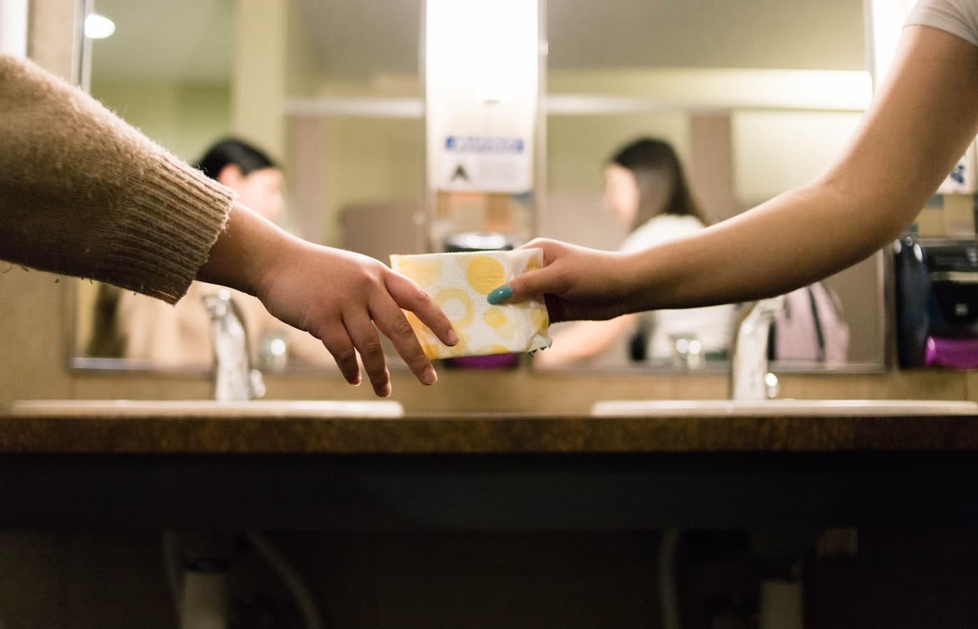 One woman passing a sanitary pad to another — support and understanding